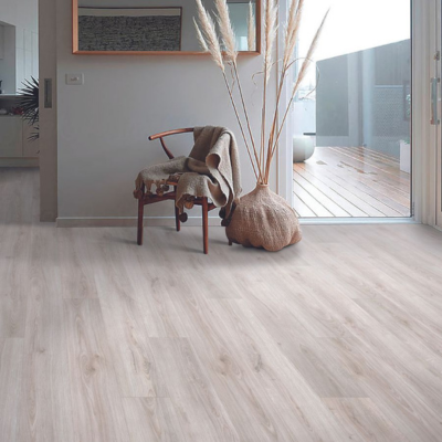 Light oak-look laminate flooring in a minimal living space with a dark wood chair, throw, pampas grass, and glass door.